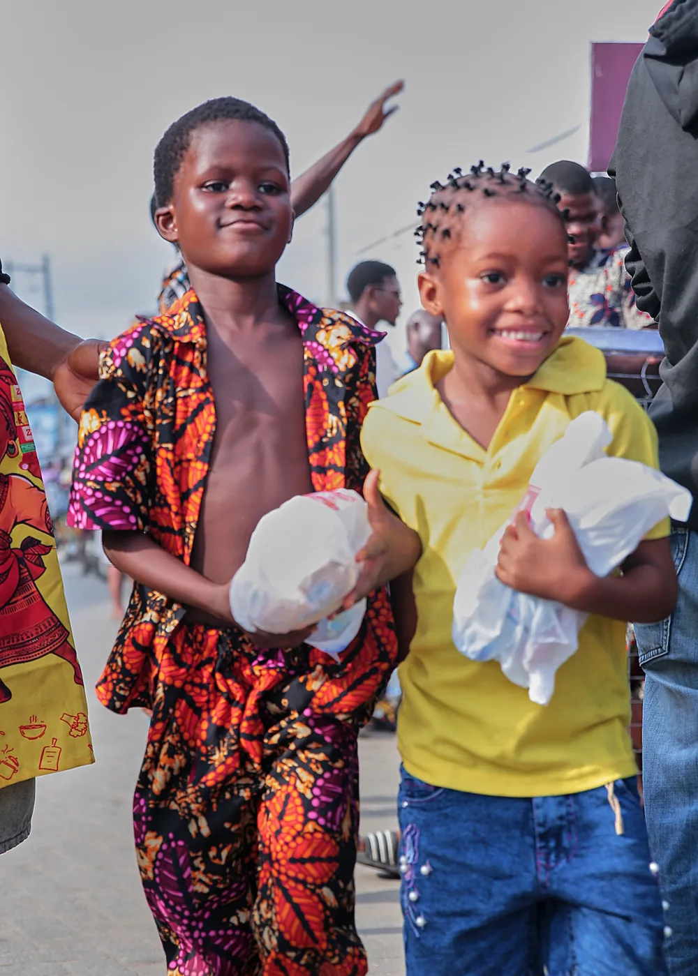 Two smiling children carrying food packs at a Sábi Chẹf event