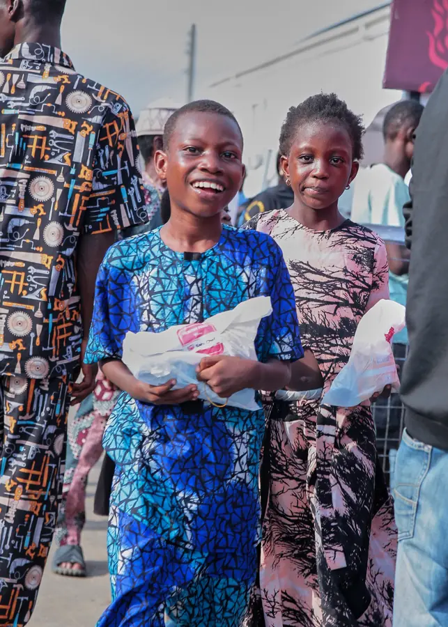 Two smiling children holding food packs at a community event